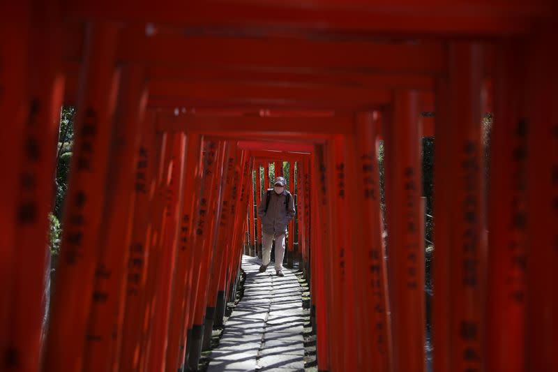 Man wearing protective face mask walks through red-coloured wooden torii gates at the Nezu shrine in Tokyo