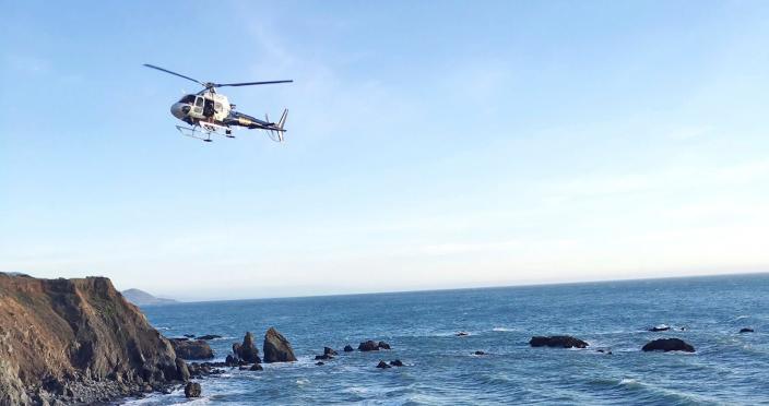 A helicopter hovers over steep coastal cliffs, near Mendocino, Calif., where a vehicle, visible at lower right, plunged about 100 feet off a cliff along Highway 1, killing five passengers.