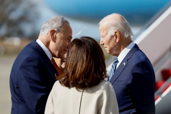 Sen. Chuck Schumer leans in to tell President Biden something crucial, beside the gangway of Air Force One. Gov. Kathy Hochul has her back to the camera.