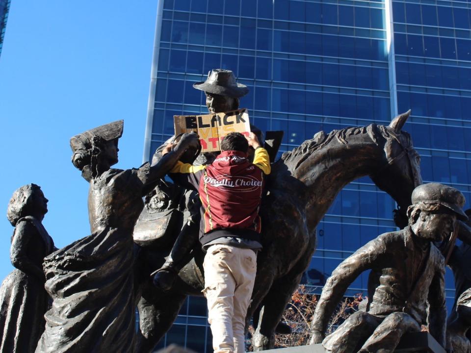 A demonstrator in Brisbane places a Black Lives Matter sign on a statue, on June 6, 2020.