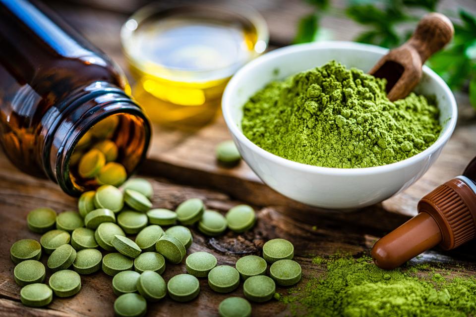 Green tea supplements pouring out of a brown jar, and a white bowl filled with green tea powder. 