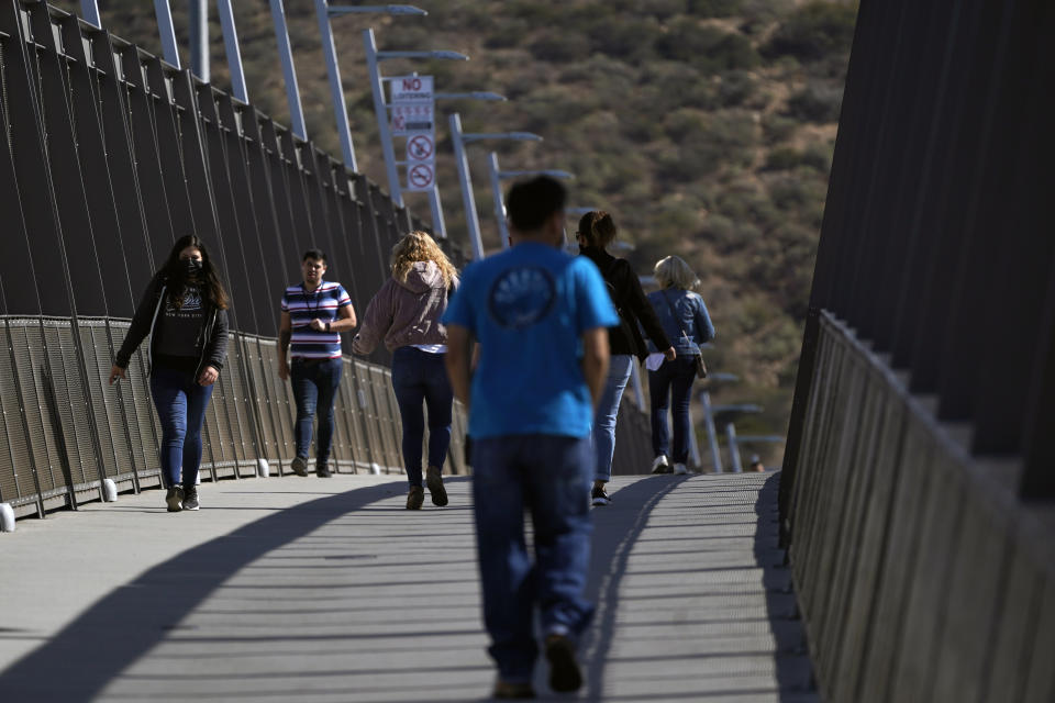 People walk on a bridge at the San Ysidro Port of Entry, connecting Tijuana, Mexico, to the United States, Wednesday, Oct. 13, 2021, in San Diego. Beleaguered business owners and families separated by COVID-19 restrictions rejoiced Wednesday after the U.S. said it will reopen its land borders to nonessential travel next month, ending a 19-month freeze. (AP Photo/Gregory Bull)