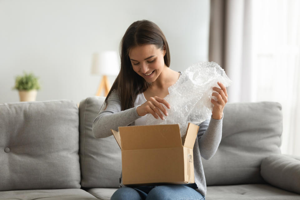 Happy young woman open cardboard box satisfied with purchase online shop order sit on sofa at home, smiling lady customer receive unpack parcel look inside, postal shipping courier service concept