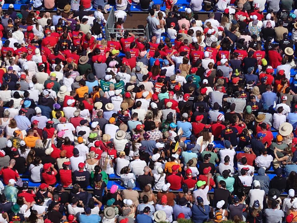 Vogelperspektive auf mehrere Fans, viele von ihnen in knallroten Hemden, auf den Tribünen während des Grand-Prix-Rennens. Die Zuschauer stehen dicht beieinander und tragen bunte T-Shirts und Hüte