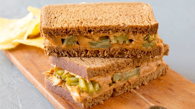 Two halves of a peanut butter and pickle sandwich stacked on a cutting board