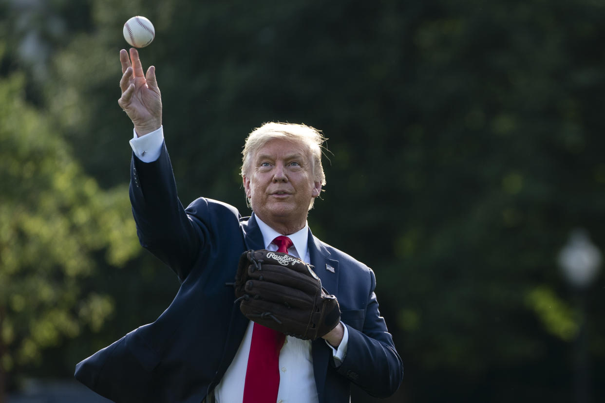 Donald Trump, in a suit and with a baseball glove, throws a baseball.