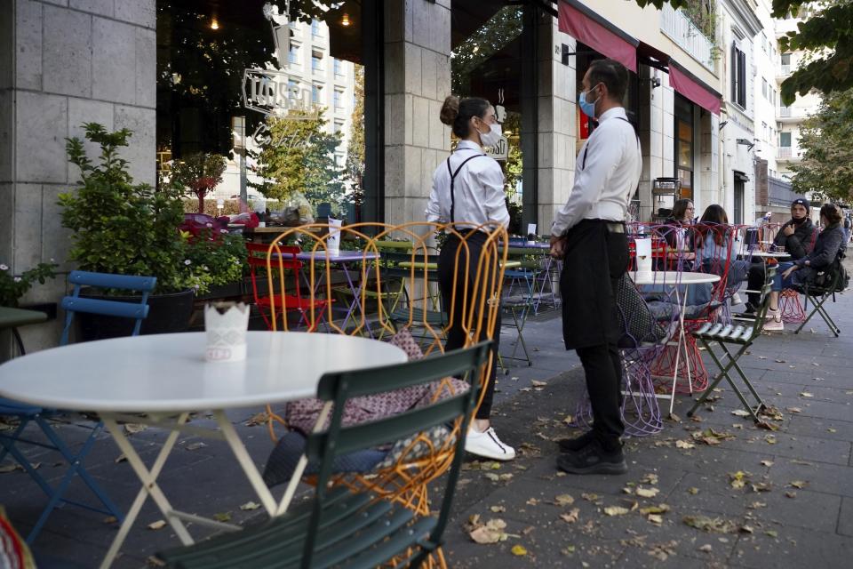 FILE - In this Oct. 13, 2020, file photo, a waiter and a waitress in masks wait for clients in Rome. After shutdowns swept nations during the first surge of the coronavirus earlier this year, some nations and U.S. states are trying more targeted measures as cases rise again around the world, especially in Europe and the Americas. (AP Photo/Andrew Medichini, File)