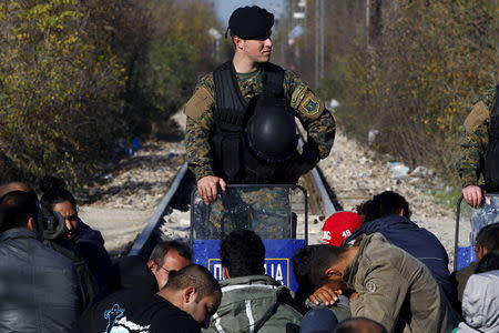 Migrants wait on the Greek side of the border with Macedonia as a Macedonian policeman stands guard on the Macedonian side, near the Greek village of Idomeni, November 19, 2015. REUTERS/Alexandros Avramidis