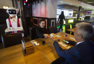 Owners Shu Lei Hu, left, and her husband Shao Song Hu, right, demonstrate the use of robots for serving purposes or for dirty dishes collection, as part of a tryout of measures to respect social distancing and help curb the spread of the COVID-19 coronavirus, at the family's Royal Palace restaurant in Renesse, south-western Netherlands, Wednesday, May 27, 2020. (AP Photo/Peter Dejong)