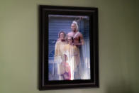 Troy Currence is reflected in a photo of himself with his mother, Hazel Harding Currence, left, and his daughter, Kendall Currence, three generations of Herring Pond Wampanoag tribal members, at his home in Bourne, Mass., Monday, Sept. 21, 2020. In August, Native descendants from all over New England and beyond were set to converge on Plymouth for The Ancestors March, listed as a "signature event" on the Plymouth 400 calendar. "We were looking forward to it so we could actually speak our truth," he says. "That we're still here. We're not a destroyed people." The coronavirus, which has disproportionately impacted Native communities across the country, has also put these plans on hold. Currence takes it as a sign. "Eventually, if you don't take care of Mother Earth and live in balance," he says, "the natural law is always going to win." (AP Photo/David Goldman)