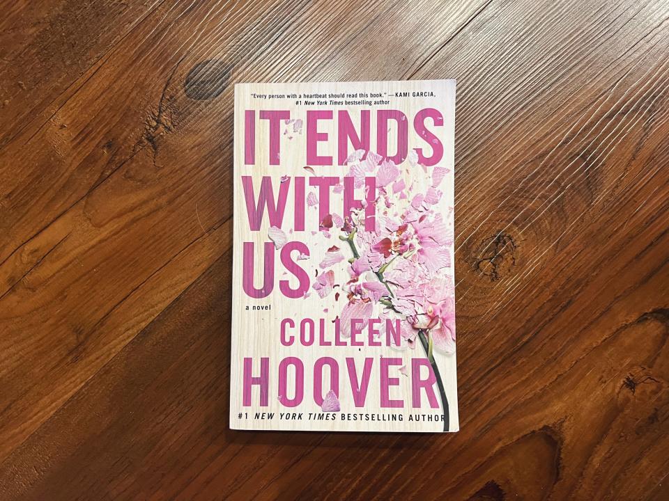 The image shows the book 'It Ends With Us' by Colleen Hoover lying on a wooden surface