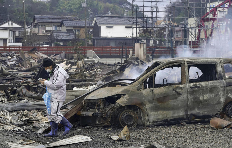 People walks past a burnt-out vehicle in an area hit by a fire, following earthquakes in Wajima, Ishikawa prefecture, Japan Wednesday, Jan. 3, 2024. A series of powerful earthquakes that hit western Japan left multiple people dead Wednesday, as rescue workers fought to save those feared trapped under the rubble of collapsed buildings.(Kyodo News via AP)