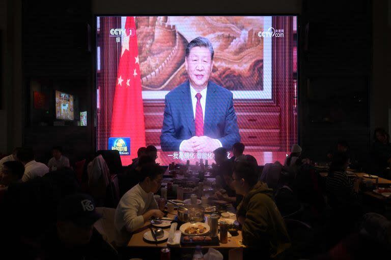 People have their dinner at a restaurant as a screen broadcasts China's President Xi Jinping while delivering his New Year's speech in Beijing on December 31, 2023. (Photo by Pedro Pardo / AFP)