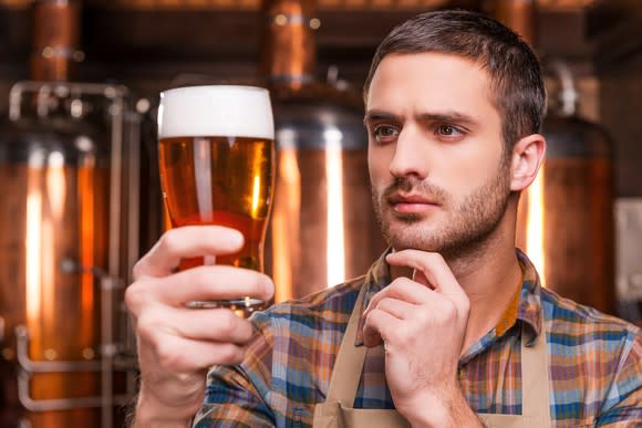 A brewer holding a pint of beer and carefully examining it.