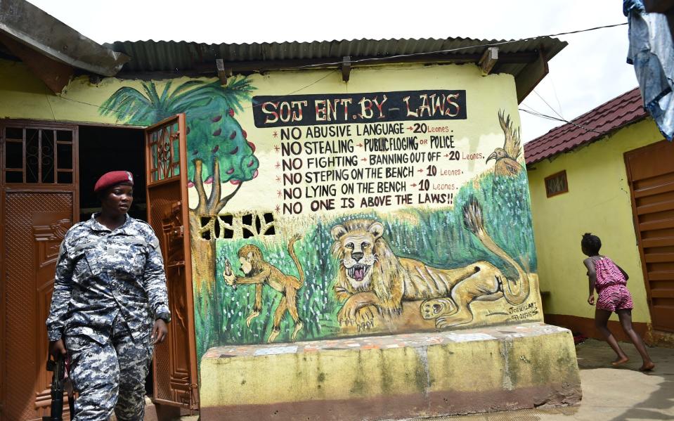 A police officer walks into a kush den with byelaws for addicts written on the wall during a raid in Waterloo a suburb outside Freetown