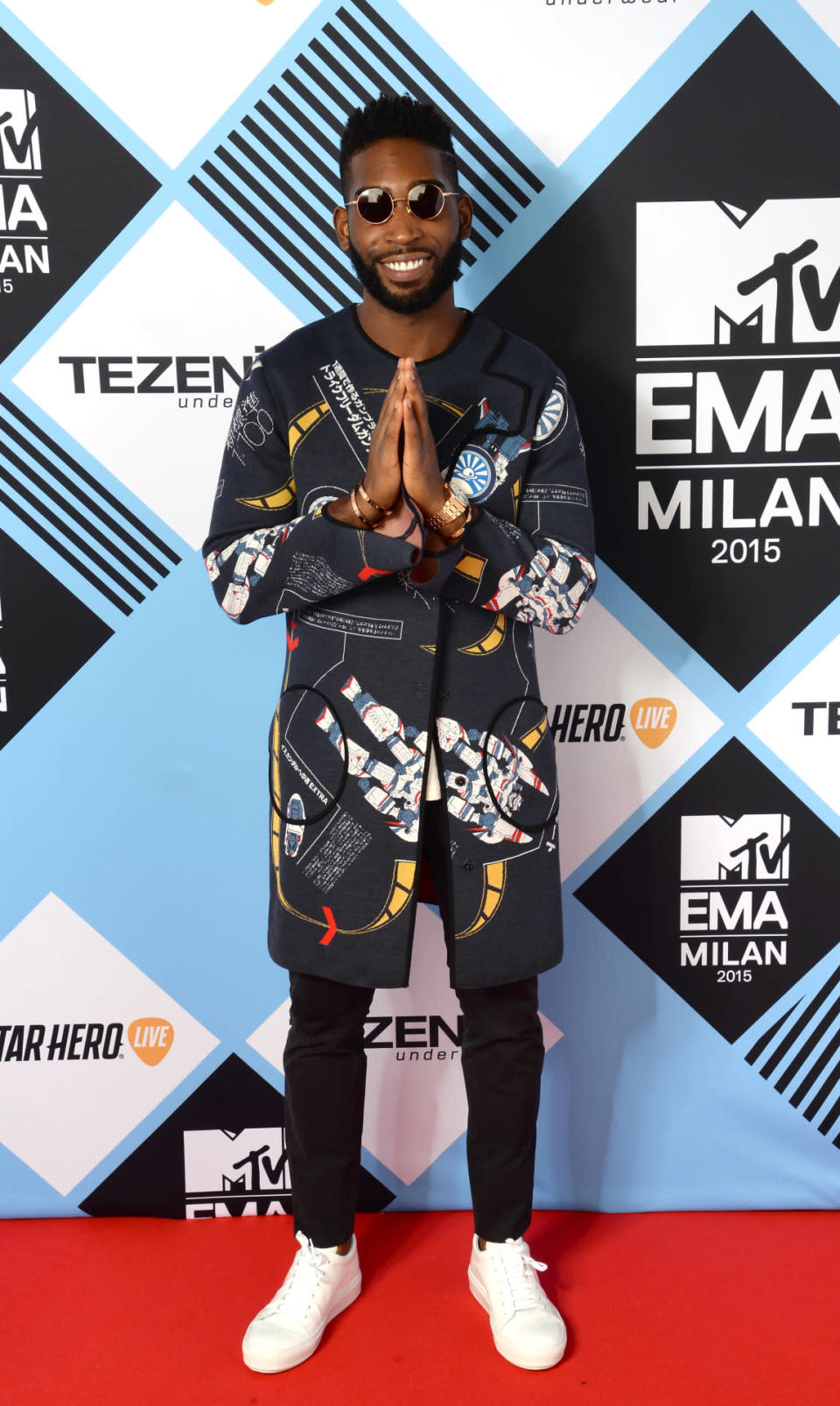 Tinie Tempah wears a graphic coat and round glasses.