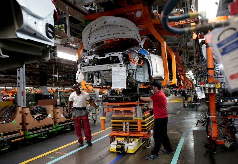 General Motors assembly workers connect a battery pack underneath a partially assembled Chevrolet Bolt EV vehicle