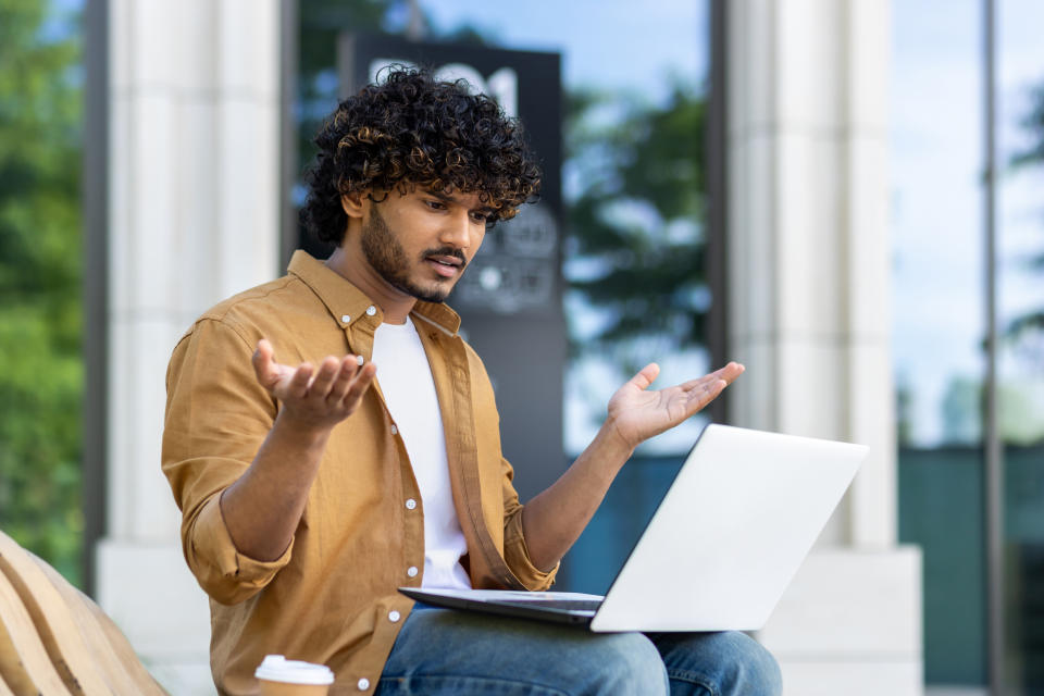 Man gesturing with confusion at laptop outdoors