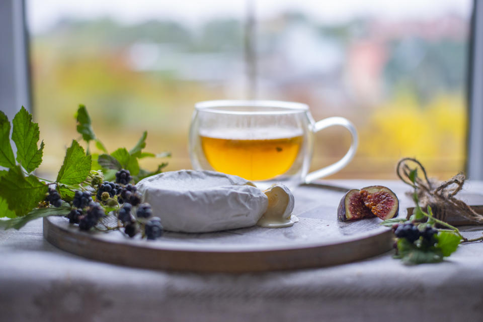 A cheese platter with figs, berries, and a cup of tea on a windowsill