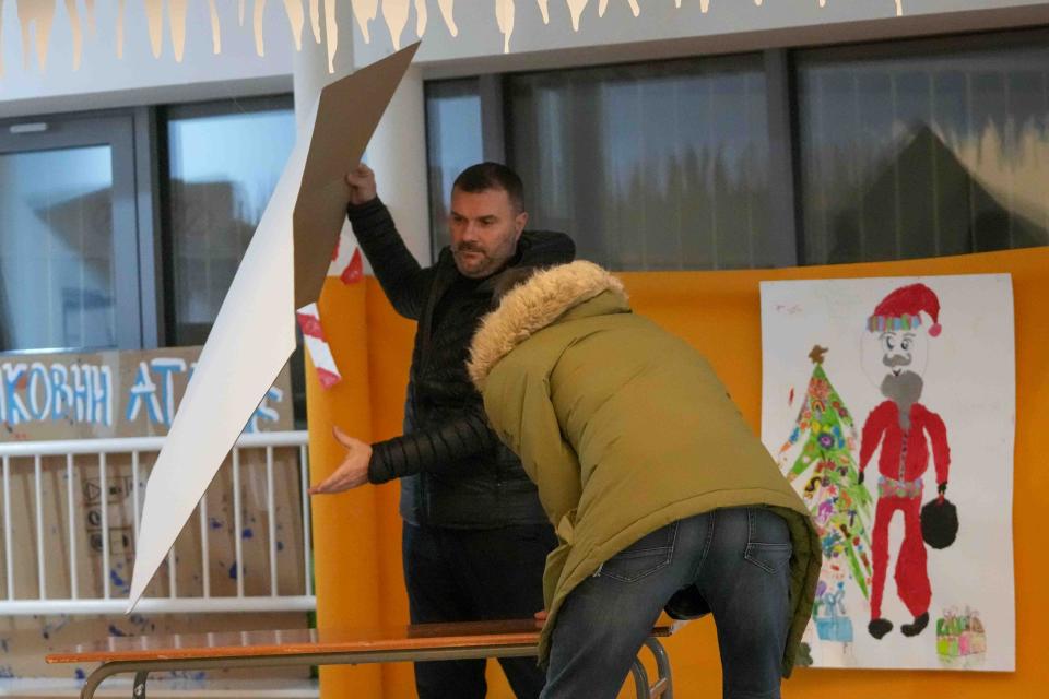 Members of the electoral commission prepare a polling station for a parliamentary and local election in Belgrade, Serbia, Sunday, Dec. 17, 2023. The vote in Serbia pits Serbian President Aleksandar Vucic's governing Serbian Progressive Party, or SNS, against a pro-Western opposition coalition which is trying to undermine the firm grip on power the populists have maintained since 2012. (AP Photo/Darko Vojinovic)