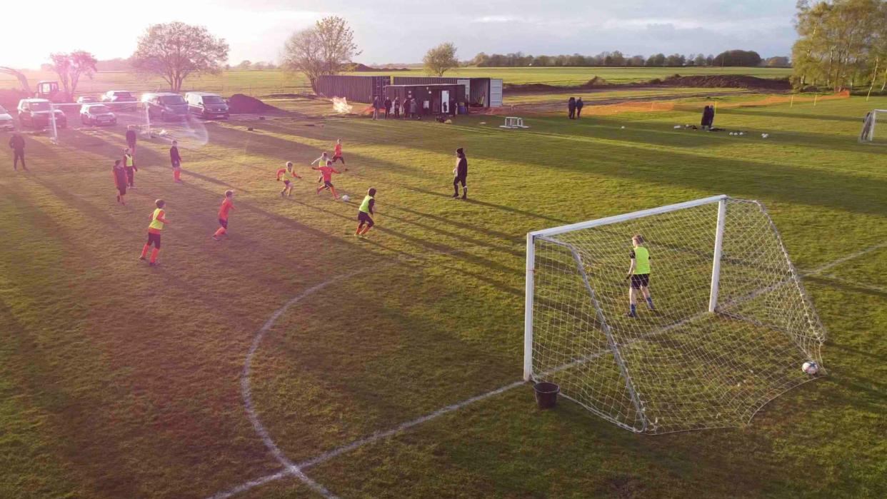 An aerial view of footballers playing on a pitch as the sun sets in the background
