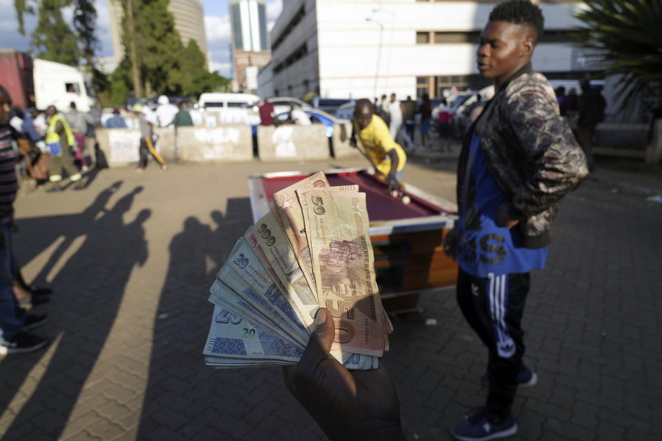 A person holds banknotes as people play pool in an open space in Harare, Zimbabwe, Wednesday, Nov. 30, 2022. Previously a minority and elite sport in Zimbabwe, the game has increased in popularity over the years, first as a pastime and now as a survival mode for many in a country where employment is hard to come by. (AP Photo/Tsvangirayi Mukwazhi)