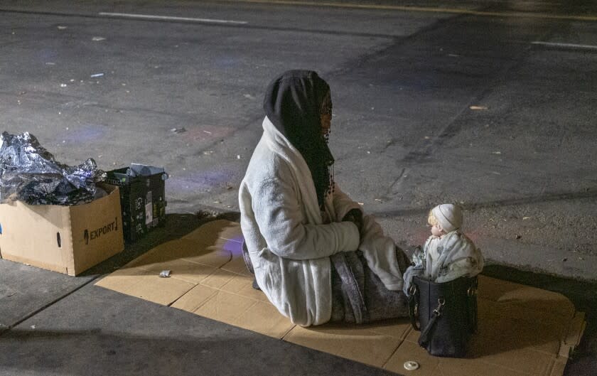 LOS ANGELES, CA - APRIL 22: A woman sits next to a doll balanced on her purse on the sidewalk in the skidrow area in the early morning hours Thursday, April 22, 2021 in Los Angeles, CA. (Francine Orr / Los Angeles Times)