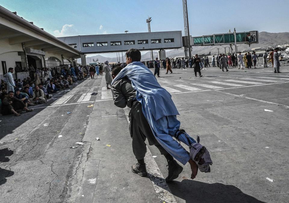 A volunteer carries an injured man as other people can be seen waiting at the airport in Kabul, Afghanistan, on Monday. (Photo by Wakil Koshar/AFP via Getty Images)