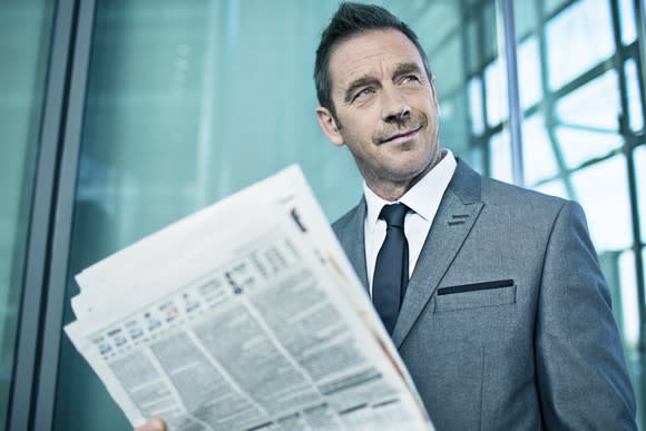 A smirking businessman in a suit holding the financial section of the newspaper.