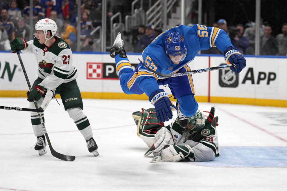St. Louis Blues' Colton Parayko (55) flies over Minnesota Wild goaltender Marc-Andre Fleury (29) as Wild's Marco Rossi (23) looks away during overtime of an NHL hockey game Saturday, March 16, 2024, in St. Louis. (AP Photo/Jeff Roberson)