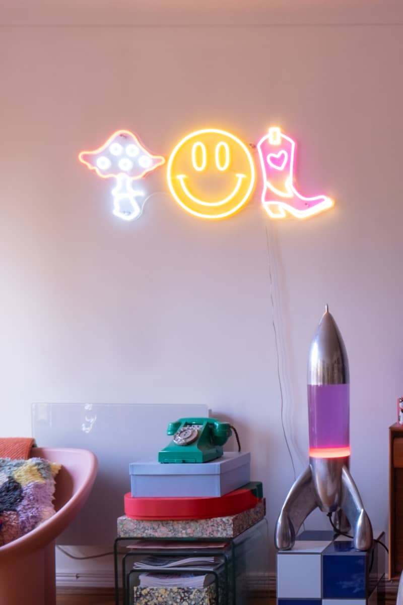 Neon signs and lava lamp decorate white room.