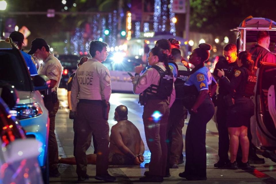 A man sits on the ground handcuffed after witnesses say he appeared to be brandishing a knife on Sunday, March 19, 2023, in Miami Beach.