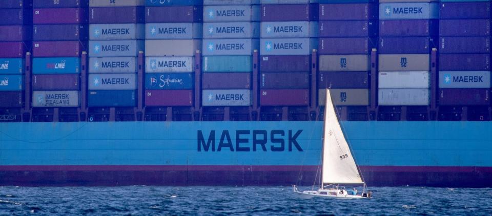 A sailboat on the water in front of a container vessel