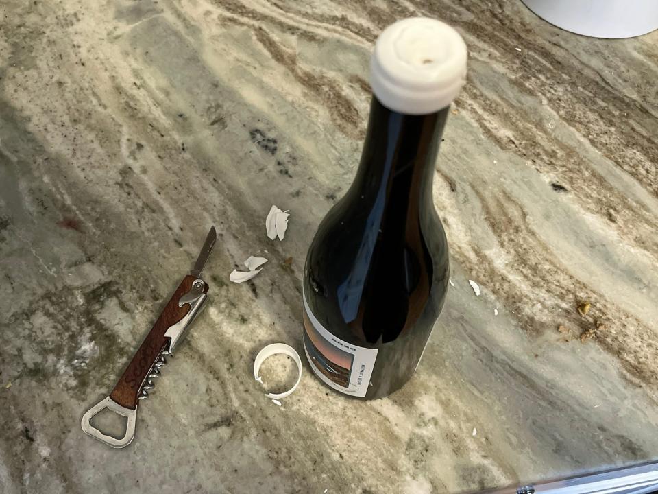 A bottle of wine with a wax seal sits on a counter, surrounded by scraps of wax and a bottle opener.