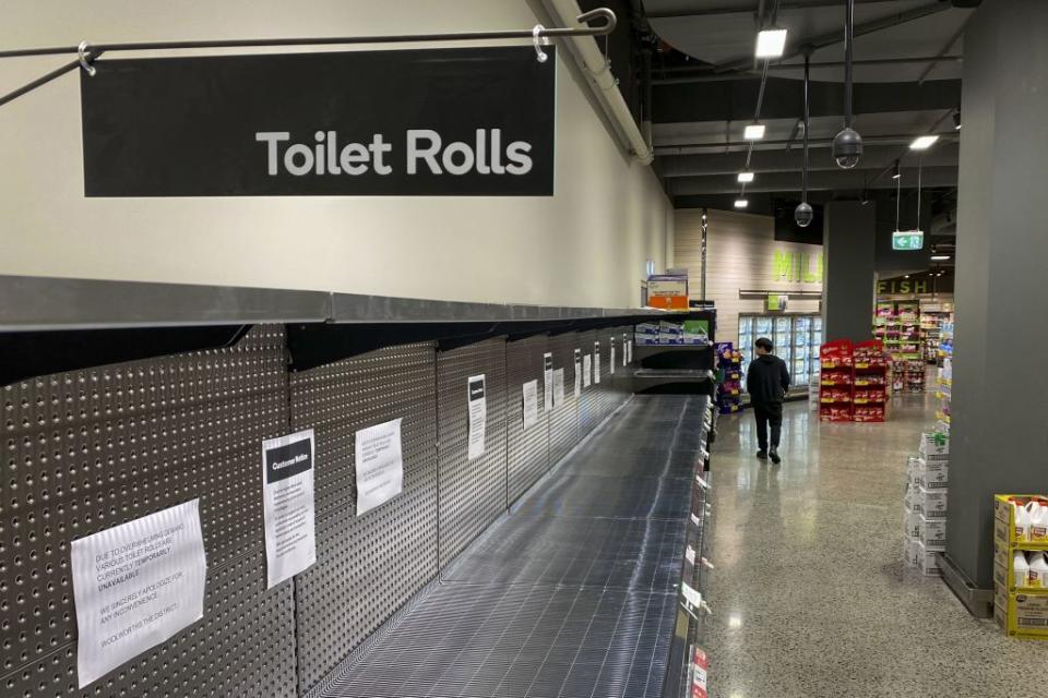 A shopper passes empty shelves usually stocked with toilet paper in a supermarket in Melbourne.