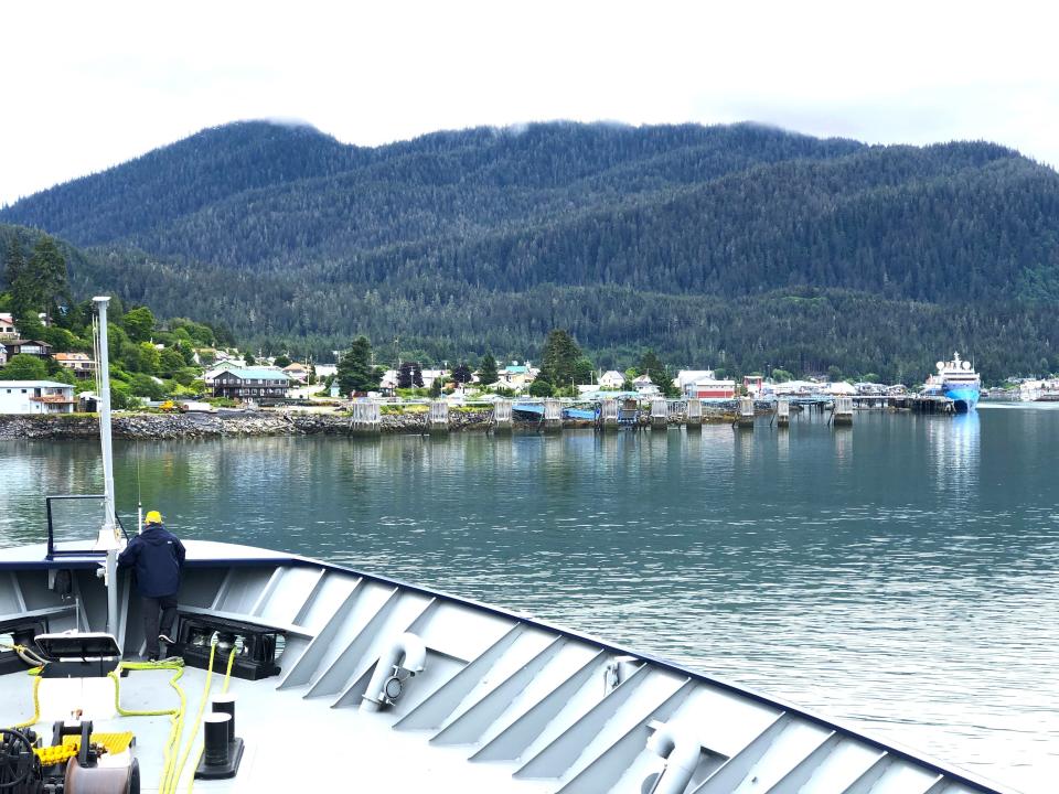 The bow of a ship with the coastline of a small Alaska town ahead in the distance.