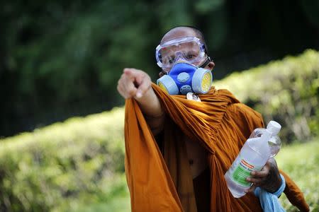 A Buddhist monk wearing a gas mask points towards police positions as they clash with anti-government protesters near the Government House in Bangkok in this December 2, 2013 file photo. REUTERS/Damir Sagolj/Files