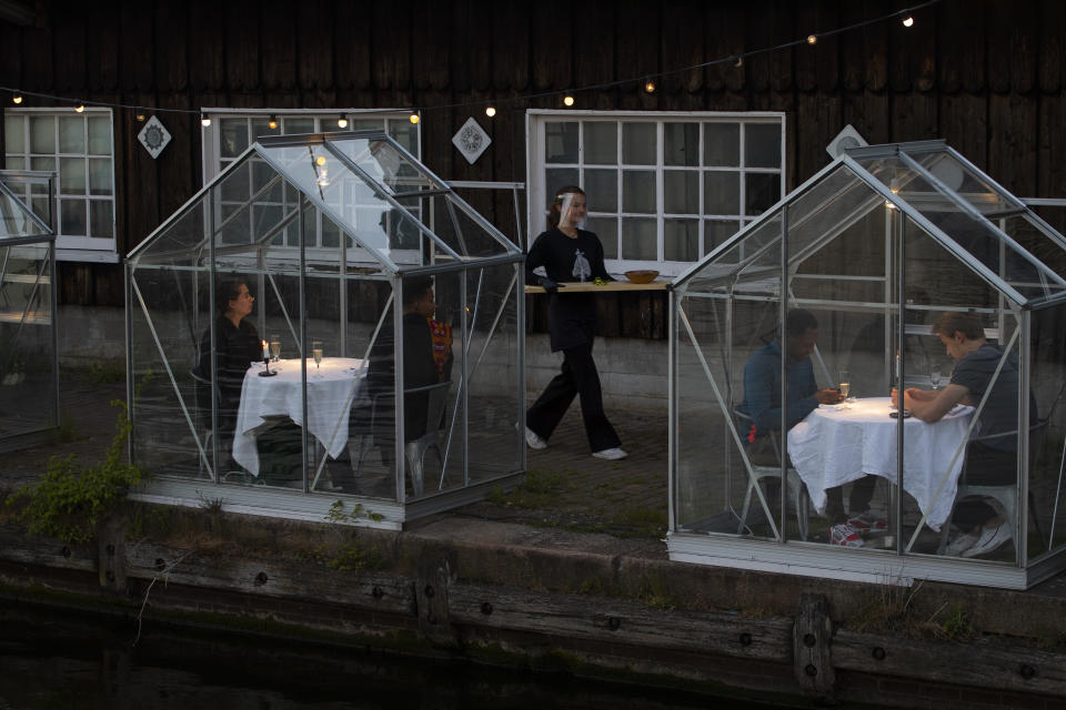 FILE - In this May 5, 2020 file photo, staff at the Mediamatic restaurant serve food to volunteers seated in small glasshouses during a try-out of a setup which respects social distancing abiding by government directives to combat the spread of the COVID-19 coronavirus in Amsterdam, Netherlands. Restaurants around the world try to lure back clientele while keeping them virus-free. (AP Photo/Peter Dejong, File)