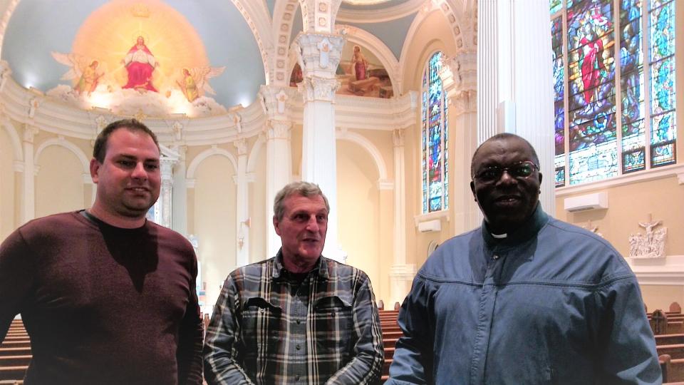 From left, Ryan Jenson, business/facilities manager for the church; John Kolly, parishioner and volunteer; and Father Charles Opondo-Owora, pastor of St. James, with the renovated worship space behind them.