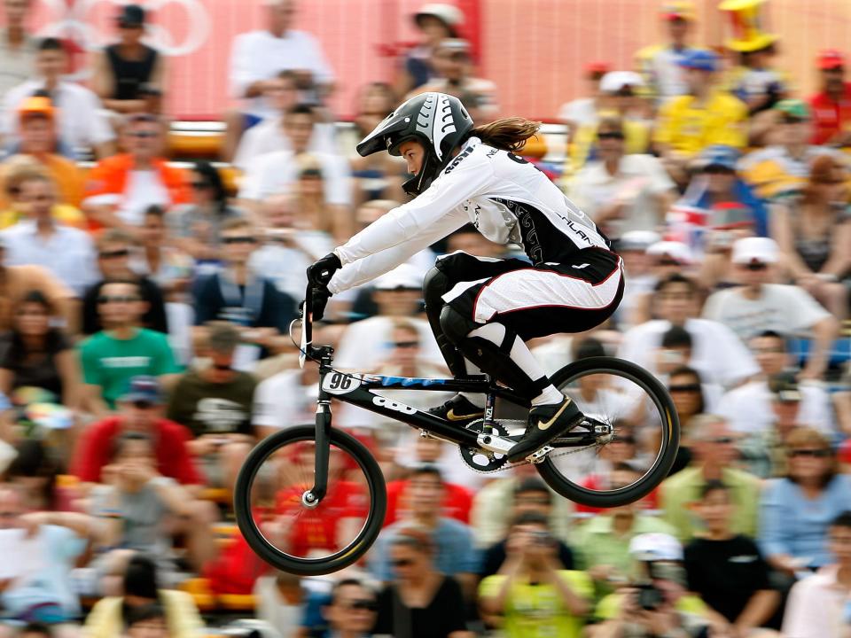 A BMX biker flies through the air with a crowd of people behind her at the 2008 Olympics.