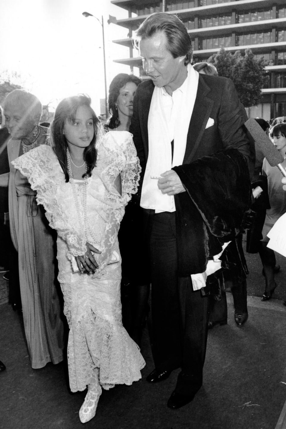 <p>Angelina Jolie est prise ici en photo aux côtés de son célèbre père, Jon Voight. Elle a 11 ans et assiste (déjà) à la cérémonie des Oscars de l’année 1986. Enfant, elle semble s’amuser dans une robe qui ressemble à s’y méprendre à une robe de mariée. Attendrissant. Crédit : Getty </p>