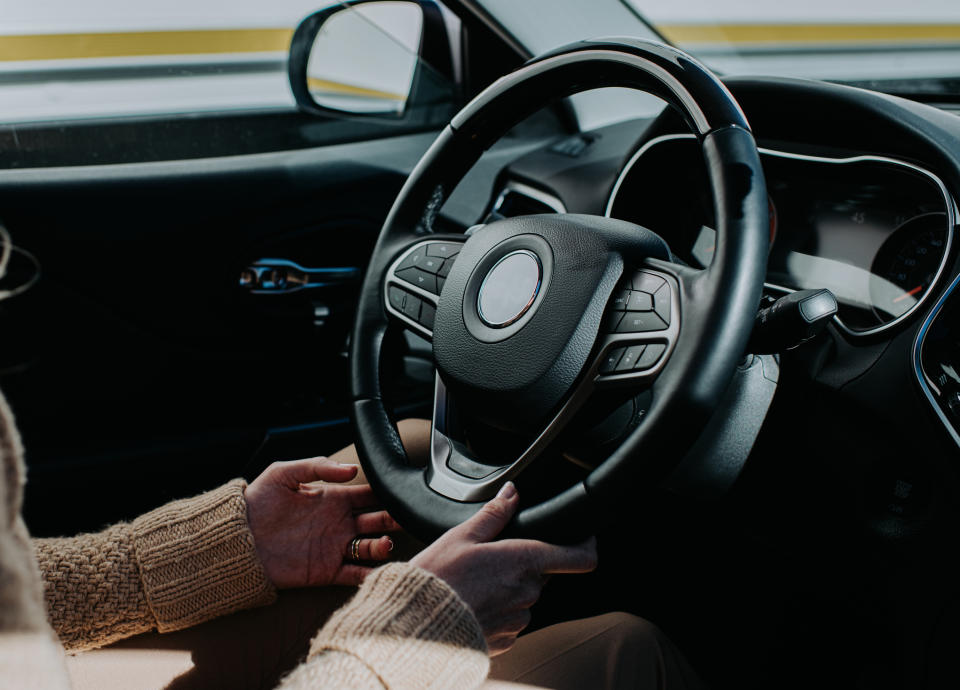 Person's hands on a steering wheel, inside a car, preparing to drive