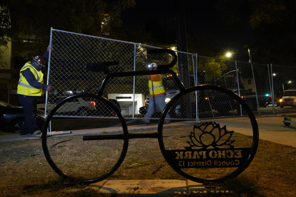 Los Angeles city contractors install a temporary fence around Echo Park Lake's perimeter in Los Angeles early Thursday, March 25, 2021. Los Angeles Police officers sweep managed to corral demonstrators gathered Wednesday to protest the planned closure of a Los Angeles park that would displace a large homeless encampment that has grown throughout the coronavirus pandemic. The park will be closed for repairs. (AP Photo/Damian Dovarganes)