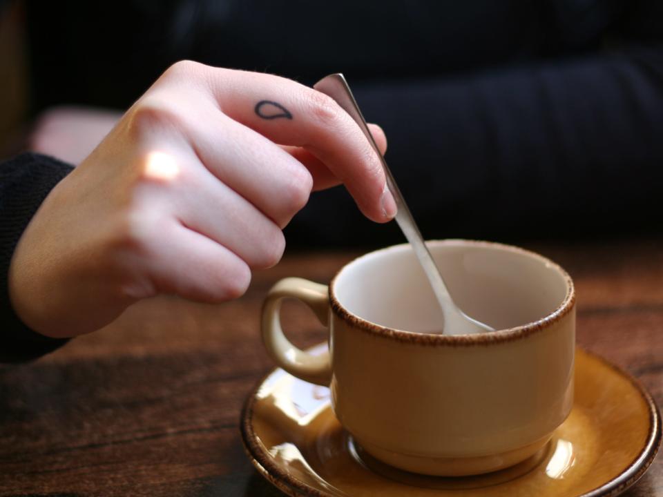 person stirring a coffee with a raindrop finger tattoo