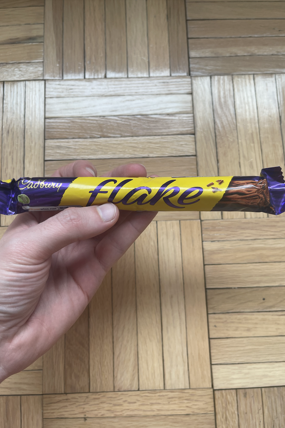 Hand holding a Cadbury Flake chocolate bar over wooden floor