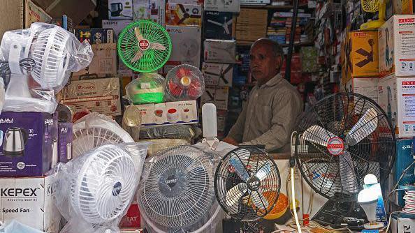 A shopkeeper selling table fans waits for customers at a market on a warm summer day in Varanasi on May 27, 2024