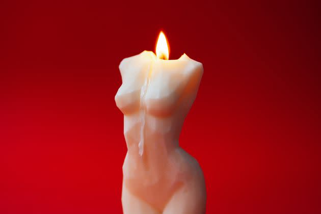 Burning soy or wax candle in shape of aesthetic female body on red background. Concept of femininity and beauty. Perfect backdrop for your design with copy space. Macro photography