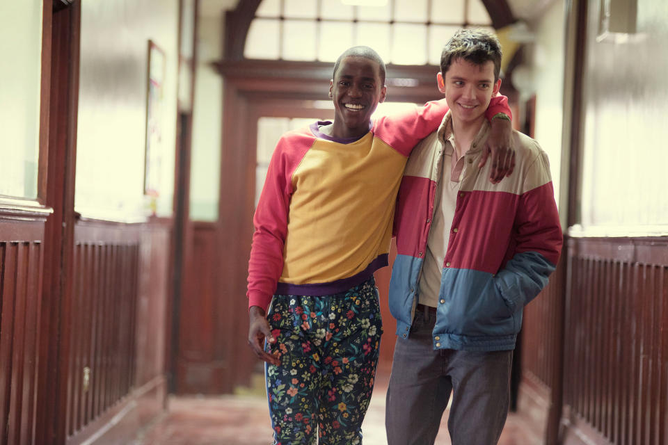 Eric and Otis smiling and walking down a hallway, Eric with an arm around Otis's shoulder