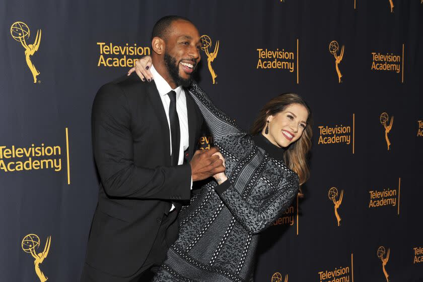 A man and a woman hugging, holding hands, smiling and posing in formal attire