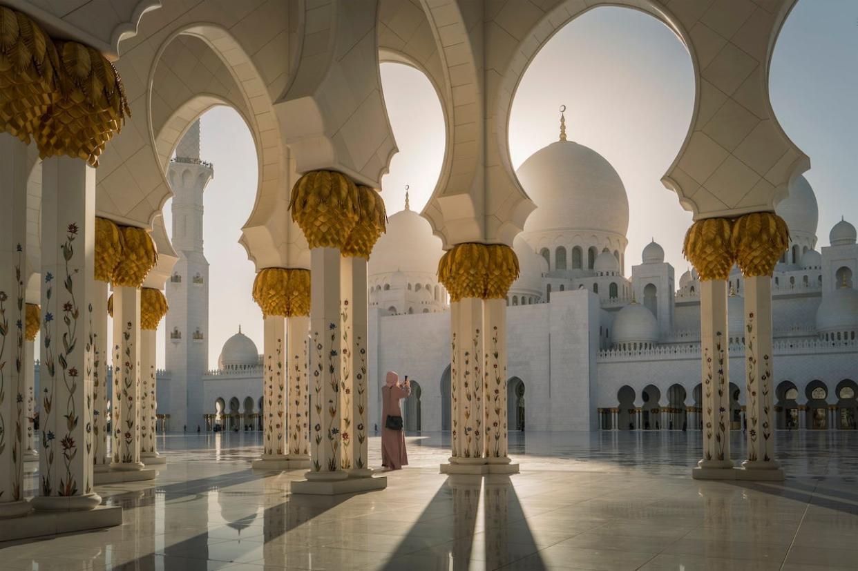 A woman taking a photograph as she stands between the white and gold pillars at Sheik Zayed Grand Mosque in Abu Dhabi.